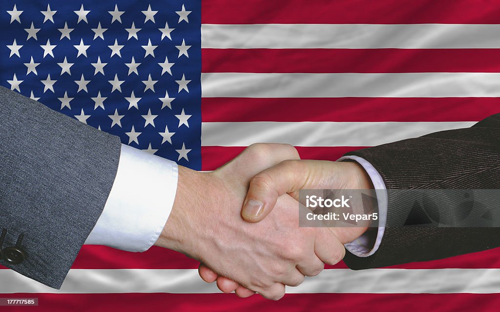 businessmen handshake after good deal in front of america flag two businessmen shaking hands after good business investment  agreement in america, in front of flag Handshake Stock Photo