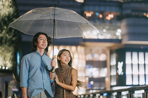 Asian Chinese couple walking in the rain with umbrella enjoying night scene in Hong Kong city street