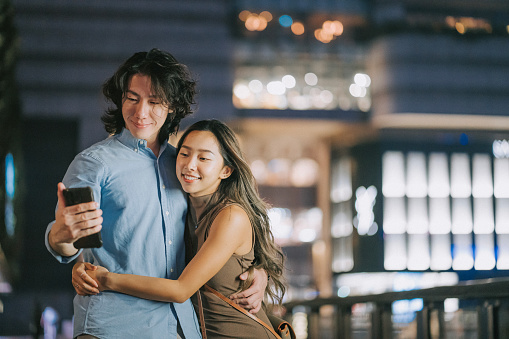 Asian Chinese couple enjoying selfie night scene in Hong Kong city street