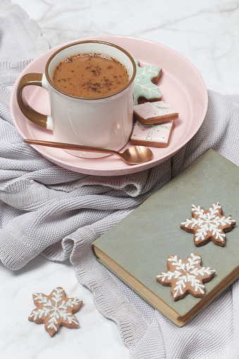 Cozy winter lifestyle concept. Mug of hot drink with vintage book and tasty homemade Christmas gingerbread cookies.