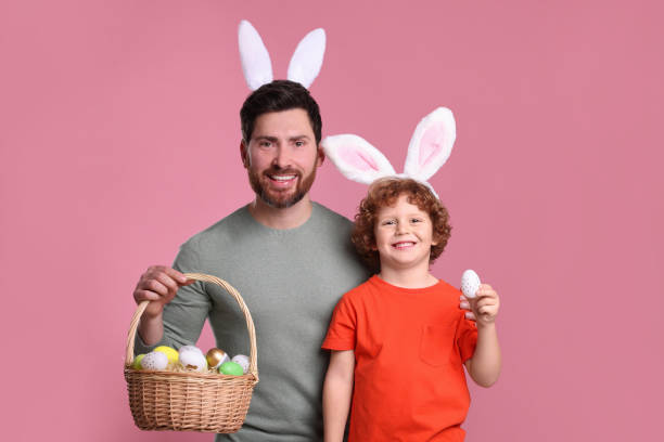 istock Happy father and son in cute bunny ears headbands holding Easter eggs on pink background 1777211091