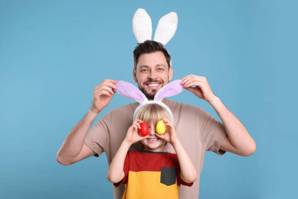 ターコイズブルーの背景で楽しんでいるウサギの耳のカチューシャの父と息子。イースターのお祝い - easter easter bunny fun humor ストックフォトと画像