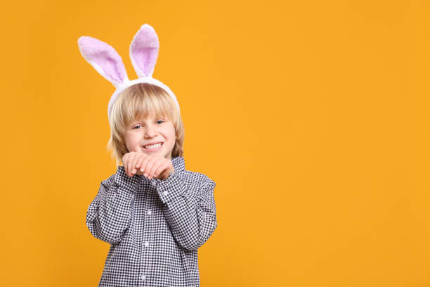 istock Happy boy wearing bunny ears headband on orange background, space for text. Easter celebration 1777213077