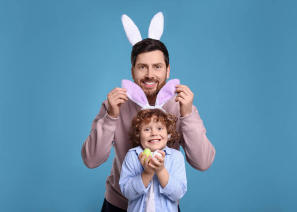 istock Happy father and son in cute bunny ears having fun on light blue background. Easter celebration 1777215816