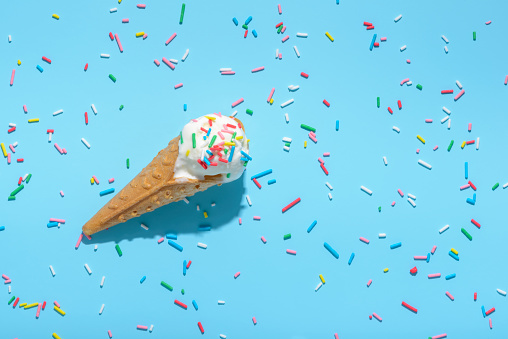 top view of ice cream cone and strewed sprinkles on blue with hard shadow, summer concept.