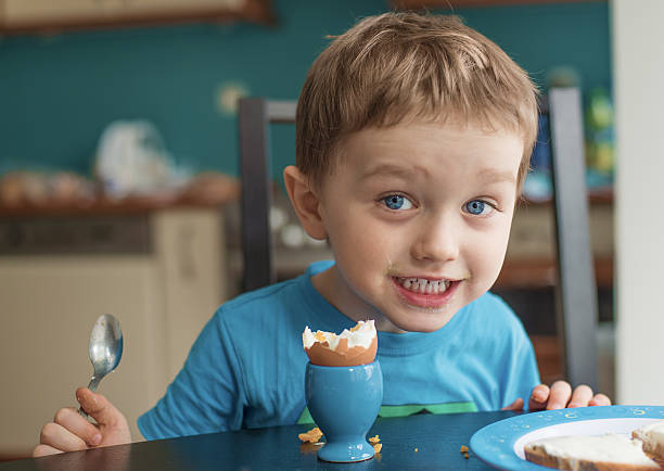 Small happy three year old boy eats an egg stock photo