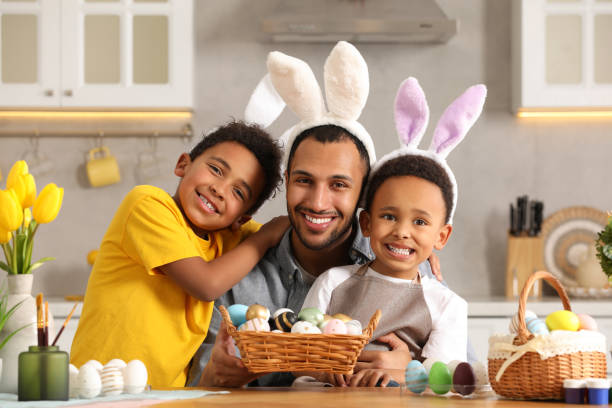 幸せなアフリカ系アメリカ人の父と彼のかわいい子供たちとイースターエッグで台所のテーブルで - bunny painting ストックフォトと画像