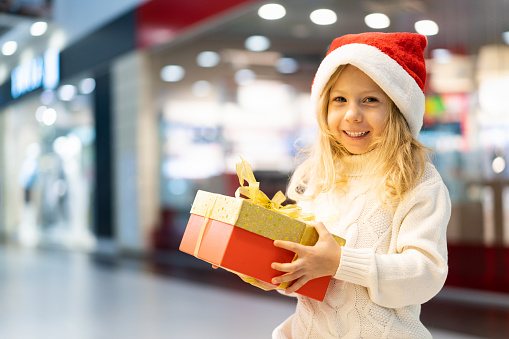 a little girl in a Christmas hat with a New Year's gift in her hands at a showcase with toys. children choose gifts for Christmas. Black Friday discounts.