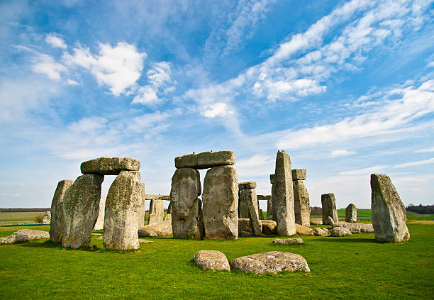 Blue skies over Stonehenge historic site The world famous prehistoric landmark and UNESCO World Heritage Site on Salisbury Plain, Wiltshire, England. A beautiful blue sky with fluffy clouds provides copy space above while bright green grasses below grab the viewer's attention. unesco world heritage site stock pictures, royalty-free photos & images