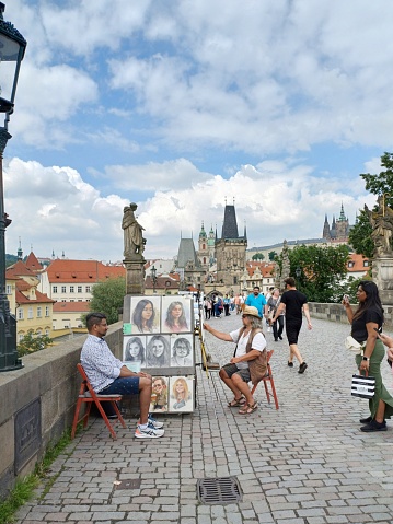 Prague, Czech Republic - June 9, 2023: People watching artists paint portraits of tourists on the Charles Bridge.