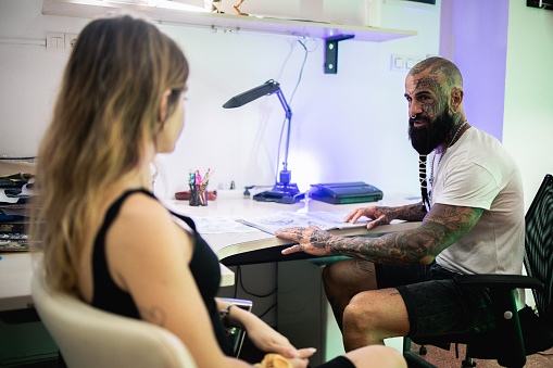 Tattoo artist and his female client discussing and planning what kind of tattoo she wants.