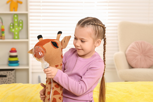 Little girl with toy giraffe and nebulizer for inhalation at home