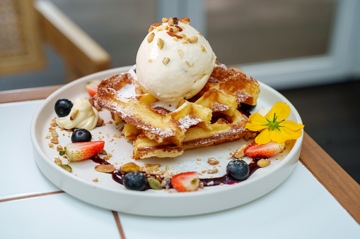 Waffle ice cream topped with fresh berries, nuts, and edible flowers