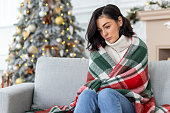 Sad lonely bored woman alone sitting on sofa at home in living room for Christmas, sad and depressed near Christmas tree, celebrating lonely new year