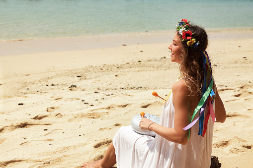 Perfect lady play relaxing melody on hapi steel tongue drum on sandy beach. Lovely woman in white playing relax music at tropical sea. Tropic summer vacation, meditating concept. Copy ad text space