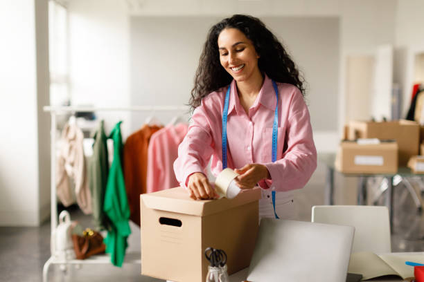 istock Cheerful Lady Designer Packing Clothes In Cardboard Box In Store 1777264317