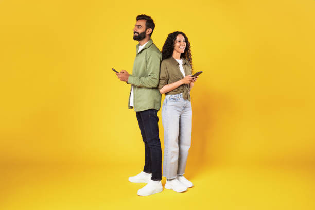 istock Middle Eastern Couple Using Cellphones Standing On Yellow Studio Background 1777277565