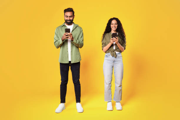 istock Smiling Middle Eastern Couple Texting Holding Smartphones On Yellow Background 1777277955