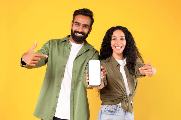 istock Excited arab couple pointing at smartphone empty screen, yellow background 1777277990