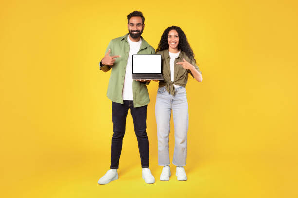 istock Smiling eastern couple holding laptop with blank screen, yellow background 1777277992