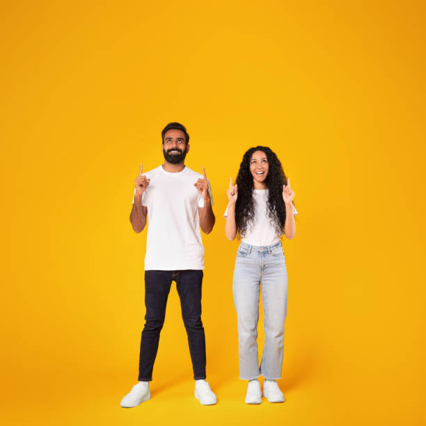 istock Excited spouses pointing fingers upward posing on yellow studio background 1777278501