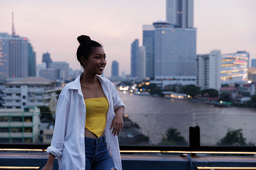 Portrait Asian woman during sunset on rooftop and river background, Bangkok Thailand