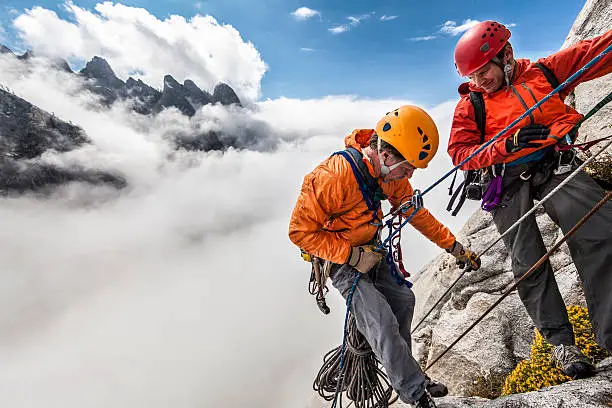 Team of climbers wearing helmets and rain gear rappelling in the clouds during a storm in Sequoia National Park.