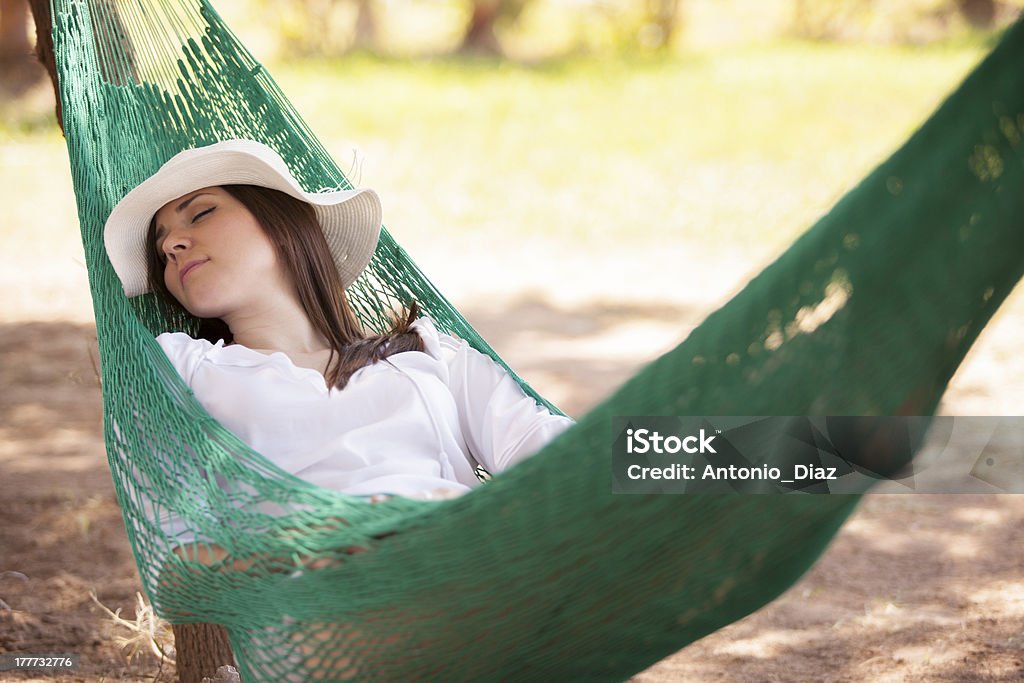 Beautiful woman resting in a hammock Young Hispanic brunette napping in a green hammock and enjoying her outdoor vacation on a sunny day Adult Stock Photo