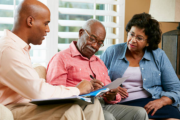 Financial Advisor Talking To Senior Couple At Home Financial Advisor Talking To Senior Couple At Home Signing Documents Sitting On Sofa form filling photos stock pictures, royalty-free photos & images