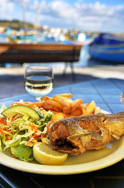 maltese fish dish backdrop of marsaxlokk village, malta. - maltese eilanden stockfoto's en -beelden