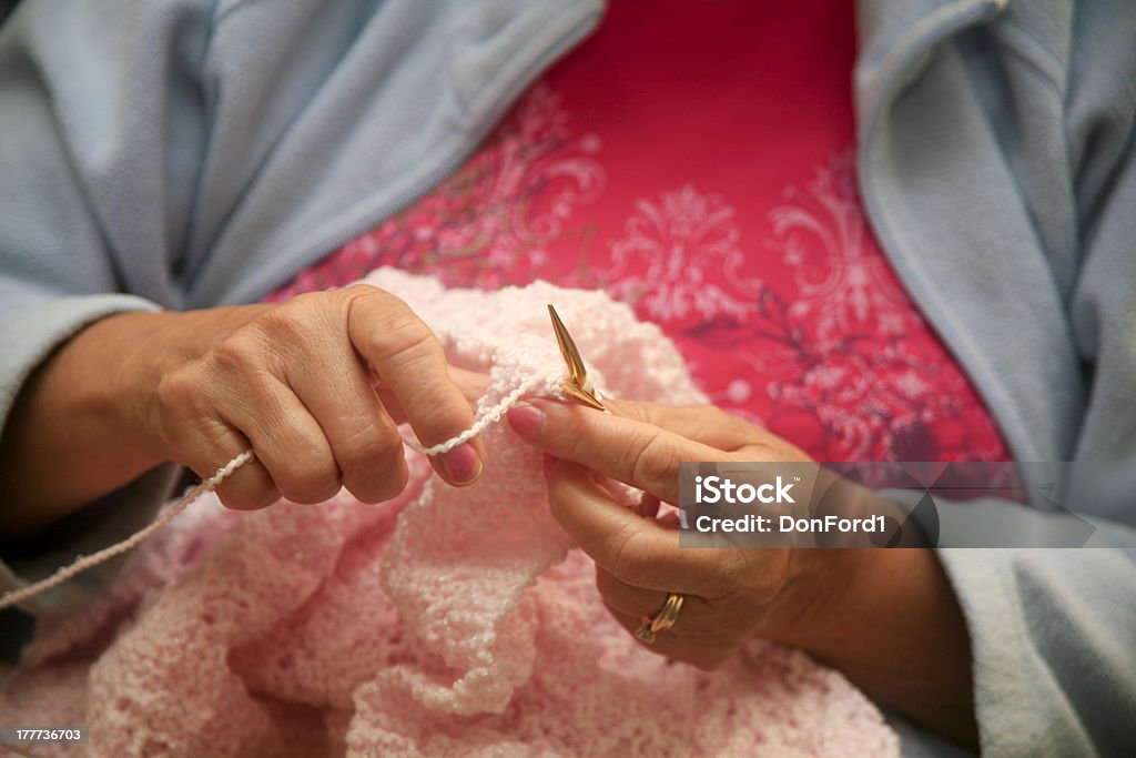 Grandmother Knitting a Pink Blanket A closeup of a grandmother knitting a pink blanket for her new grand- daughter She has beautiful hands and is wearing a light blue fleecy and a pink top.  Adult Stock Photo
