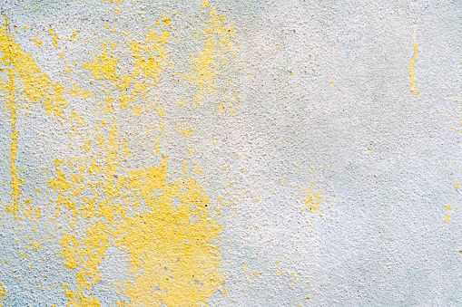 Flaking yellow blue paint on the stucco exterior wall of an old house