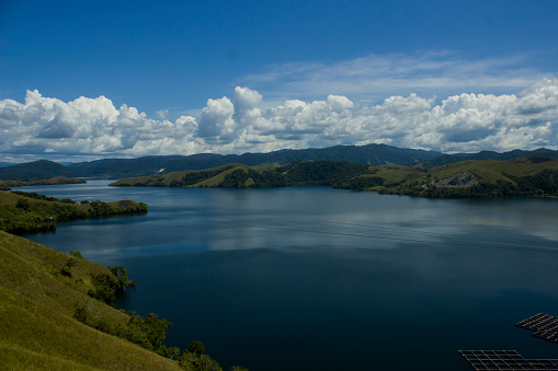Beautiful natural scenery during the day Lake Sentani, green hills, green mountains and blue sky with thick white clouds.