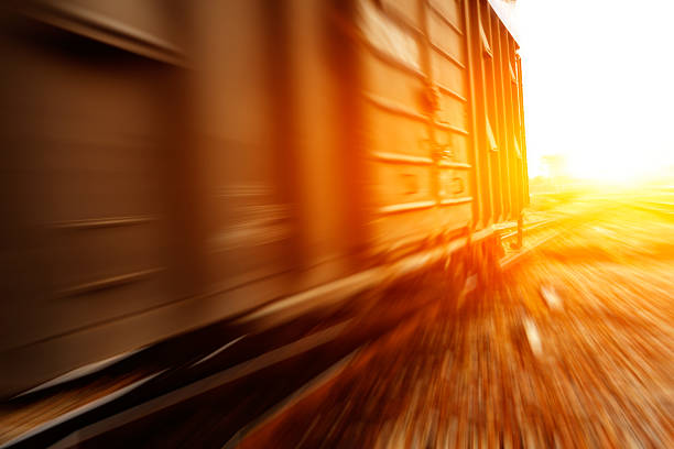 A vibrant train speeds along railway tracks, showcasing a blend of colors while structures support overhead cables. The sunlit surroundings create a bright atmosphere.