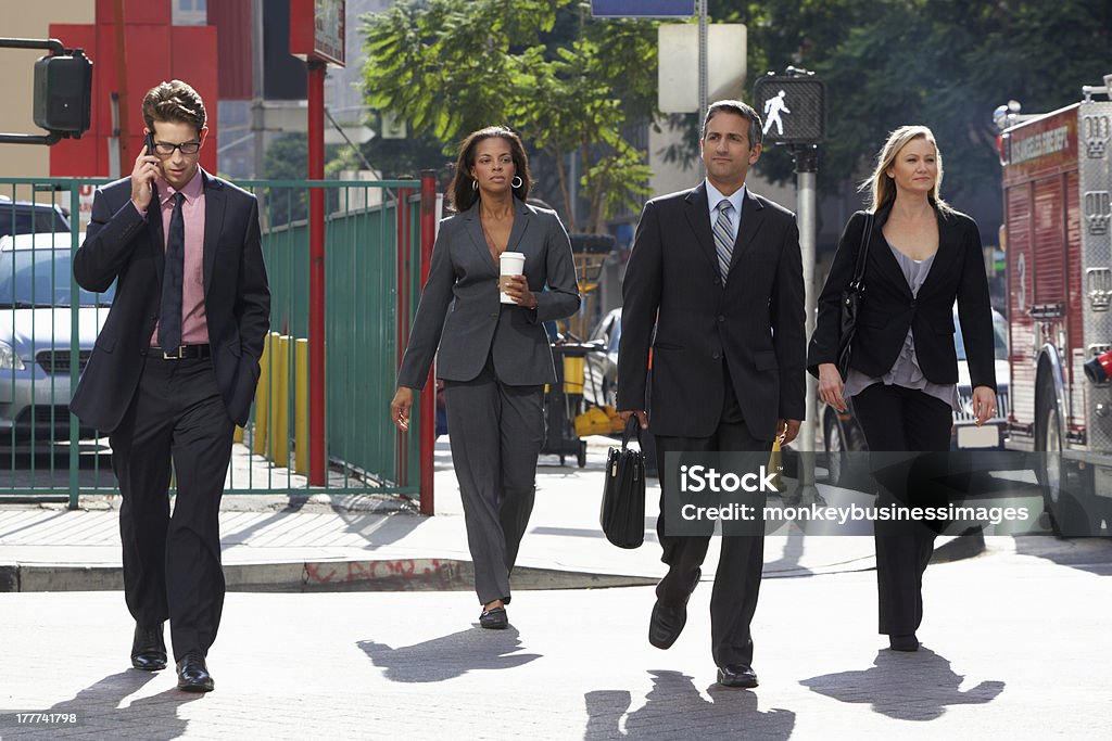 Group of elegant businesspeople crossing a street Group Of Businesspeople Crossing Busy Street Wearing Suits Holding Briefcase And Takeaway Coffee Walking Stock Photo