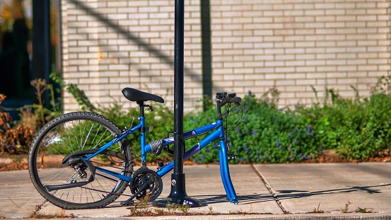 The blue bicycle is locked at the pole on the sidewalk. The front wheel is lost.