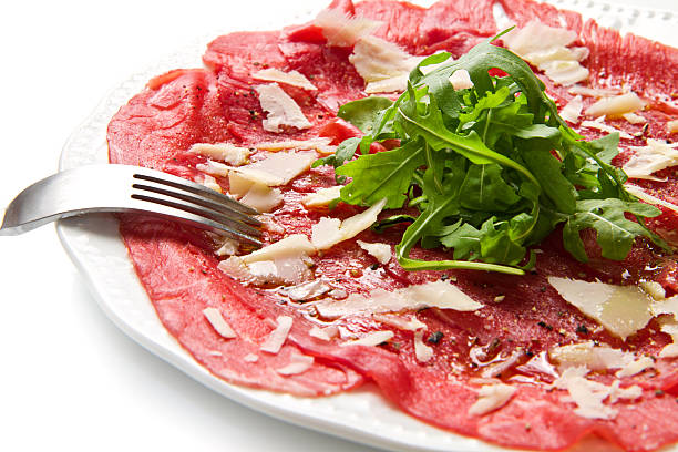 white dish with carpaccio of beef on arugula over white background