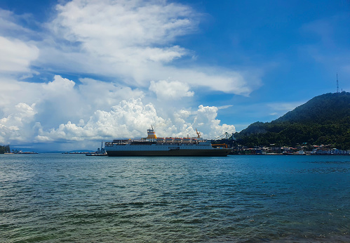View of a passenger ship docking at Jayapura harbor during the day with blue sky and white clouds.