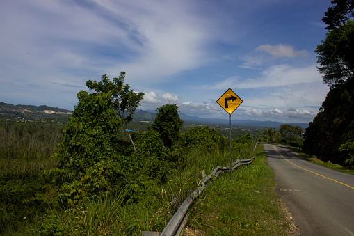 A right-turning traffic sign is stuck on the side of the road with the Koya valley in the background.