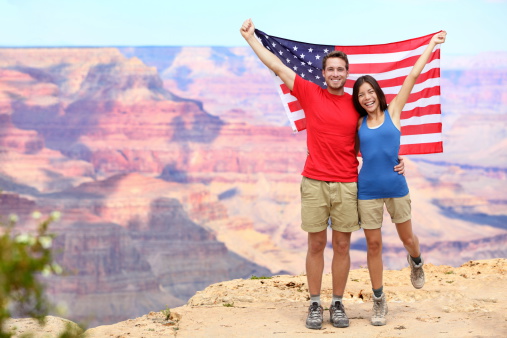 USA travel tourist couple holding american flag in Grand Canyon. Happy young multiethnic couple cheering at Grand Canyon south rim during summer holidays.