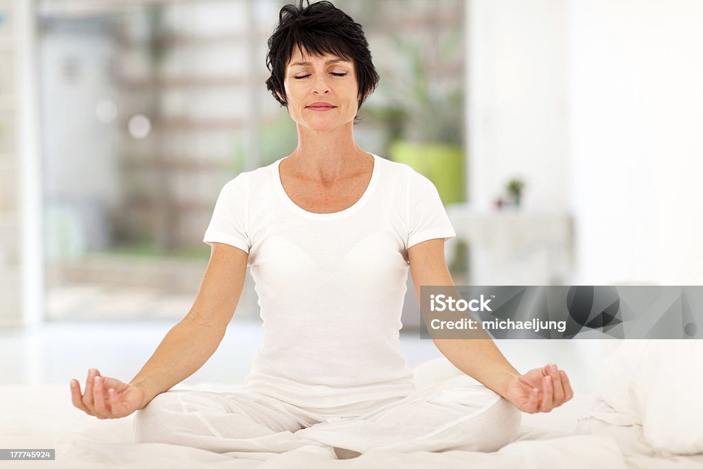 Bella metà età donna meditare sul letto - Foto stock royalty-free di Donne mature