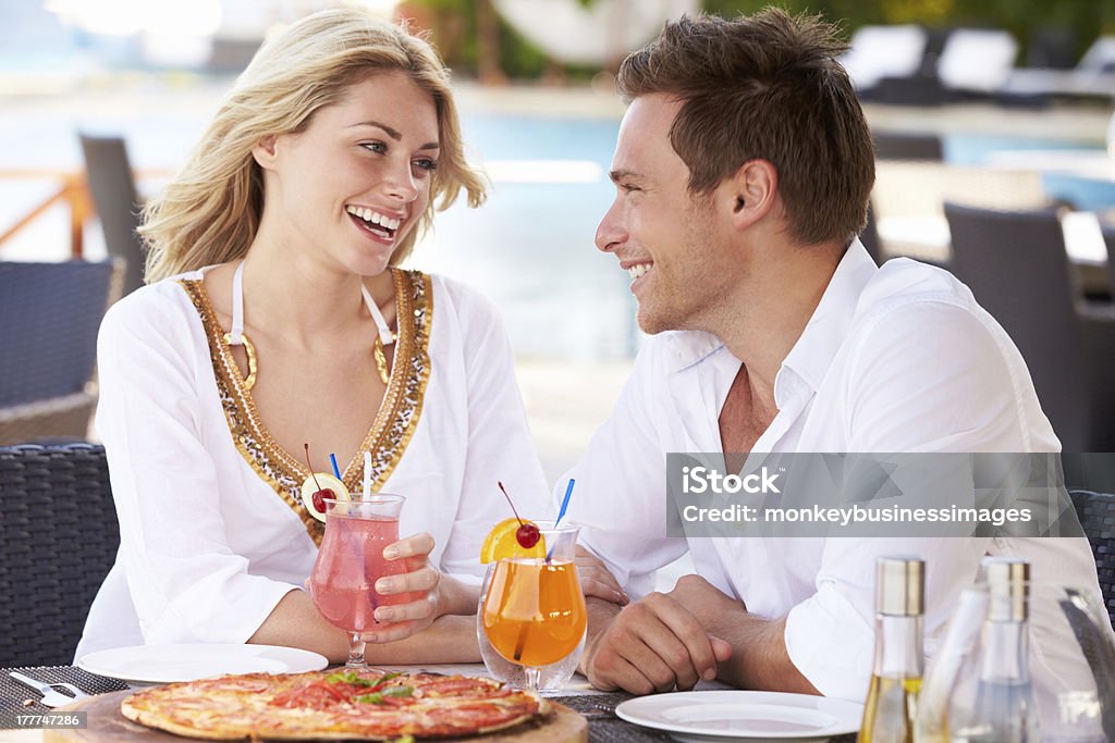 Couple eating pizza and drinking tropical drinks outside Couple Enjoying Meal In Outdoor Restaurant Looking At Each Other Smiling Couple - Relationship Stock Photo