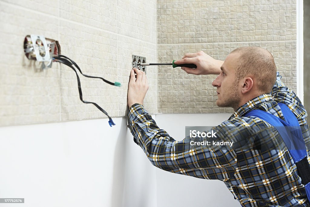 Electrician installing wall outlets Young electrician at work with wall outlet and screwdriver installing sockets Adult Stock Photo