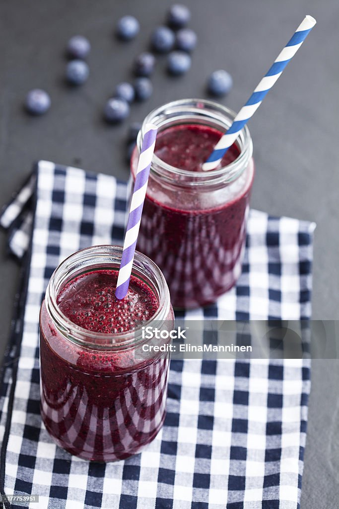 Blueberry smoothies Closeup of two blueberry smoothies in glasses with striped straws resting on checkered napkin with fresh blueberries in background Blueberry Stock Photo