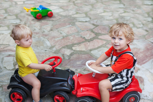 Two little brother toddlers playing with toy car in summer garden
