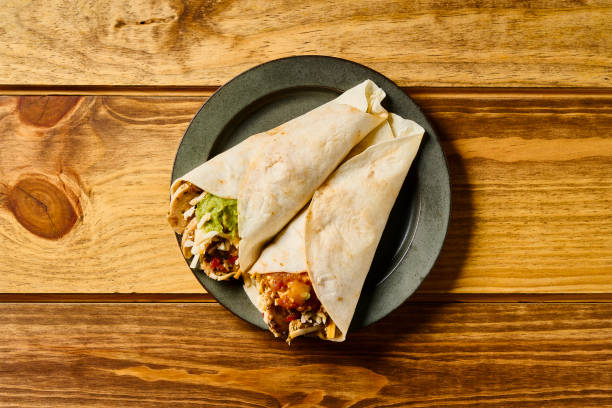 An enticing open-faced chicken burrito topped with fresh vegetables, sauces, and garnishes, presented on a wooden board, ideal for a savory and satisfying meal.