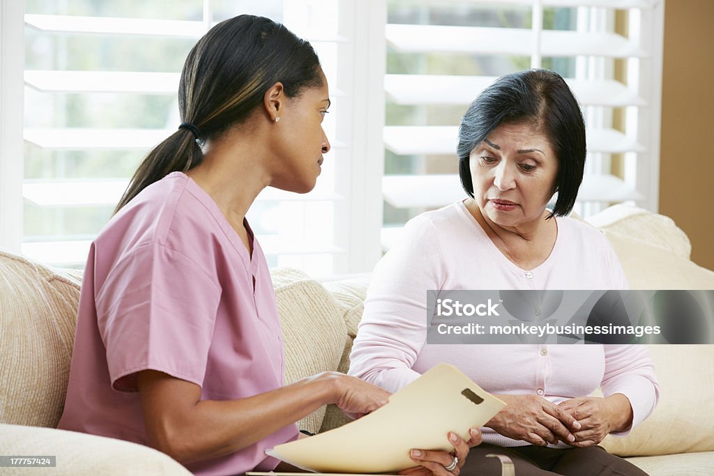 Nurse discussing records at home with senior patient Nurse Discussing Records With Senior Female Patient During Home Visit Sitting Down Reassuring Patient Stock Photo
