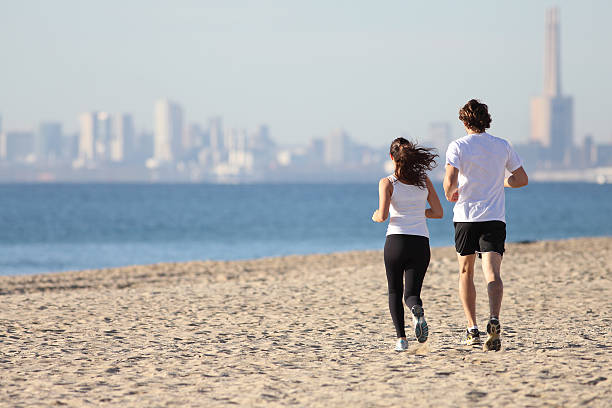 Man and woman running in the beach towards the sea with a city in background