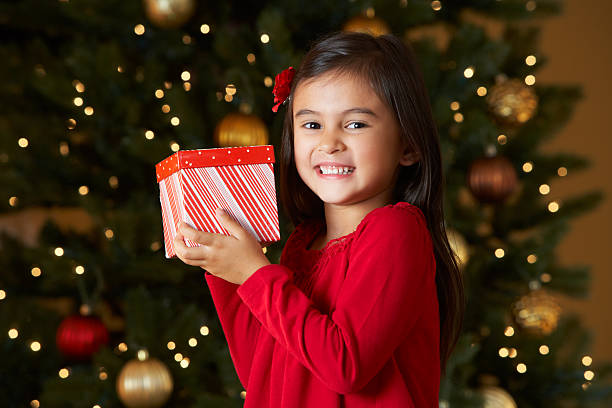 Girl holding Christmas gift with tree in background