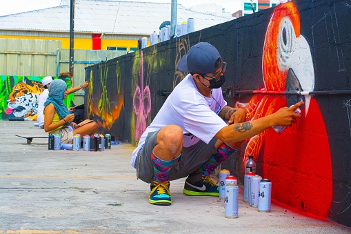 Young male artist painting graffiti on wall outdoors.